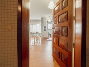 A hallway leading to a dining area with a table and chairs, a kitchen area with a stove, and a wooden door with a handle. - ESPINHO SEAWALK AND SEAVIEW by VACATIONY by Interhome (Espinho)