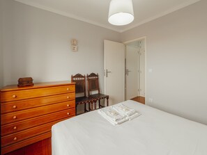 A bedroom with a wooden dresser, two chairs, a bed with white linens, and a white door. - ESPINHO SEAWALK AND SEAVIEW by VACATIONY by Interhome (Espinho)