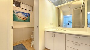 A bathroom with a toilet, a sink with a mirror, and a painting of a sea creature on the wall. - Experience true beachfront living Honolulu’s prestigious Gold Coast @ Sans Souci (Honolulu, HI)