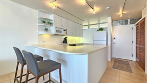 Uma cozinha moderna com ilha central, banquetas, armários brancos e micro-ondas embutido.