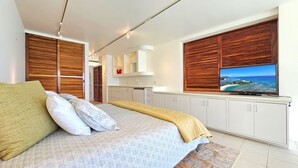 Quarto moderno com cama, persianas de madeira, uma televisão e vista para o oceano.