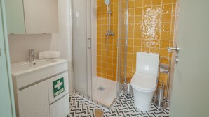 Et badeværelse med en hvid vask, et spejl, et toilet og en bruser med gul klinkevæg.