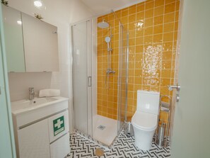 Ein Badezimmer mit einem weißen Waschbecken, einem Spiegel, einer Toilette und einer Dusche mit gelben Fliesen.