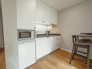 A compact kitchen with white cabinetry, a built-in microwave, a coffee maker, and a wooden floor. - Apartment  by Interhome (Porto)