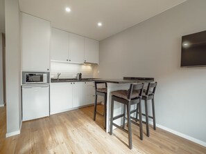 A modern kitchen with white cabinetry, a microwave, and a built-in oven. There are two bar stools with cushions. - Apartment  by Interhome (Porto)