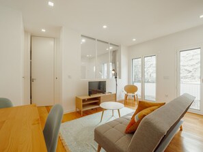 A modern living room with a wooden dining table, a sofa, a TV, and a large window. - Apartment  by Interhome (Porto)