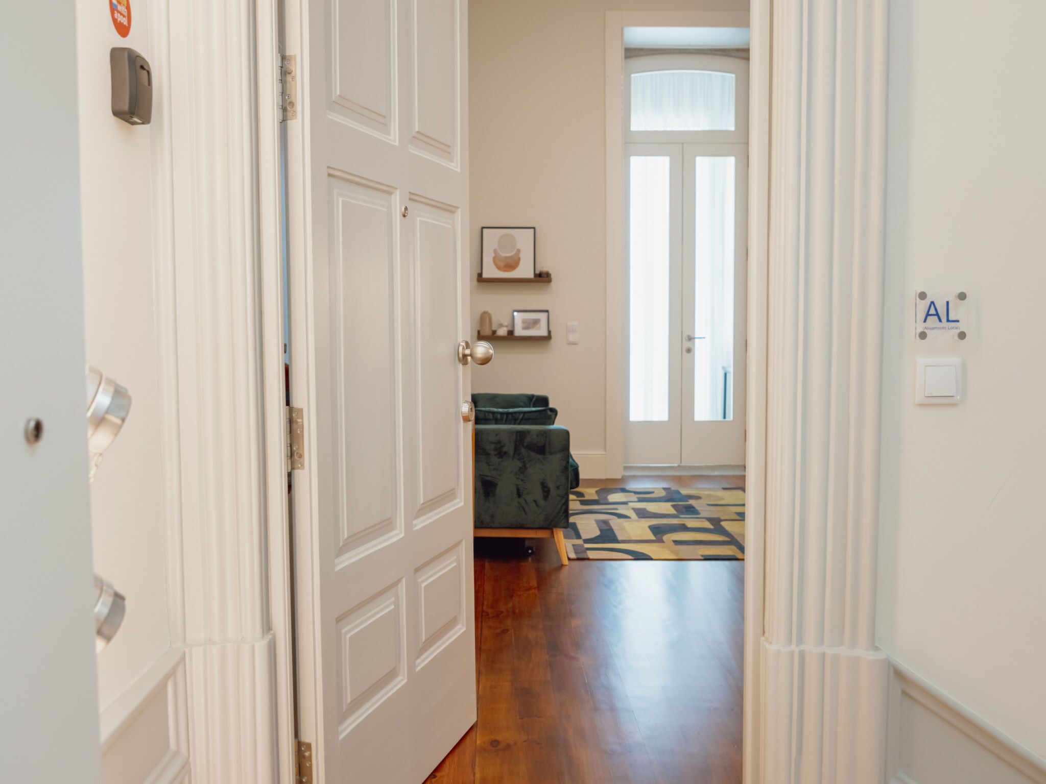 Un couloir avec un plancher en bois, un canapé vert et un tapis à motifs.