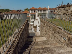 Eine Treppe führt zu einem modernen Gebäude, begleitet von einer Steinmauer auf der einen Seite und einem Metallzaun auf der anderen.