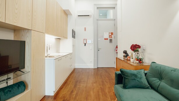 Un apartamento moderno con kitchenette, una sala de estar con sofá verde y un pasillo que conduce a una puerta.
