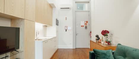 A modern apartment with a kitchenette, a living area with a green sofa, and a hallway leading to a door.
