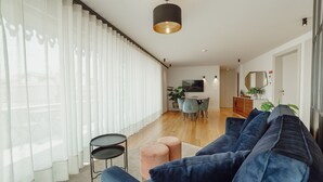 Een moderne woonkamer met een grote blauwe bank, een klein rond tafeltje en een eethoek met een televisie en stoelen.