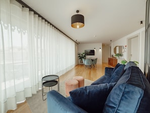 A modern living room with a large blue sofa, a small round table, and a dining area with a TV and chairs. - DOWNTOWN PENTHOUSE with RIVER VIEW by VACATIONY by Interhome (Porto)