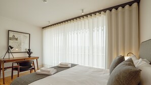 Een hotelkamer met een bed, een bureau, een stoel, een kaart aan de muur, en een raam met gordijnen.