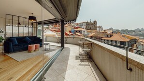 Een modern balkon met een bank en poefs, met uitzicht op een stadsgezicht met historische gebouwen.
