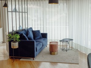A modern living room with a blue sofa, a round wooden ottoman, a small black table, and a potted plant. - DOWNTOWN PENTHOUSE with RIVER VIEW by VACATIONY by Interhome (Porto)