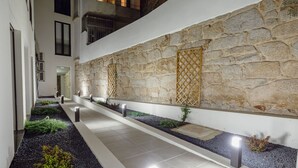 Um corredor moderno e interno com paredes de pedra, iluminação embutida e um caminho ladeado por plantas.