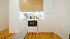 Uma cozinha compacta com armários de madeira, bancada de mármore, forno embutido e um banco.