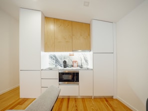 A compact kitchen with wooden cabinets, a marble countertop, a built-in oven, and a bench. - Apartment  by Interhome (Porto)