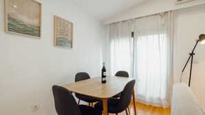 Uma área de refeições com uma mesa de madeira, quatro cadeiras, uma garrafa de vinho e duas obras de arte emolduradas na parede.