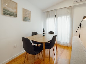 A dining area with a wooden table, four chairs, a bottle of wine, and two framed artworks on the wall. - Apartment  by Interhome (Porto)