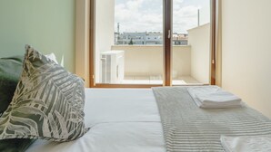 A bedroom with a bed, a window with a view of buildings, and a wall-mounted light fixture. - Apartment  by Interhome (Porto)
