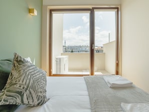 A bedroom with a bed, a window with a view of buildings, and a wall-mounted light fixture. - Apartment  by Interhome (Porto)