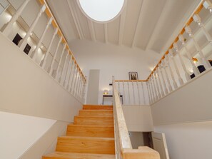 Eine Treppe mit Holzbeschlägen und weißen Wangen, die zu einer Zwischenebene mit einem runden Dachfenster führt.
