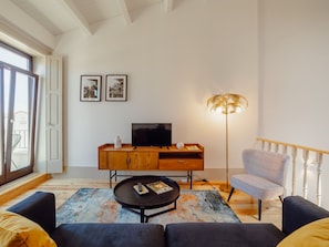 Ein Wohnzimmer mit einer Couch, einem Couchtisch, einem Fernseher, einem Schrank, einer Stehlampe und einem Sessel.