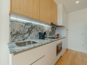 A modern kitchen with a marble countertop, stainless steel sink, and wooden cabinets. - Apartment  by Interhome (Porto)