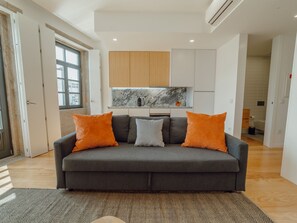 A modern living room with a grey sofa, two orange cushions, a marble backsplash, and a kitchen in the background. - Apartment  by Interhome (Porto)