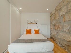 A bedroom with a bed, a stone wall, a door, and a shelf with decorative items. - Apartment  by Interhome (Porto)