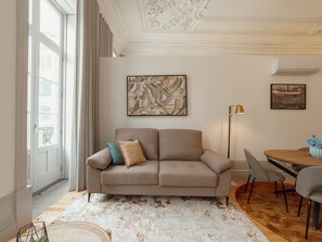 Ein modernes Wohnzimmer mit einem beigen Sofa, einem Couchtisch und einem Essbereich mit Stühlen.