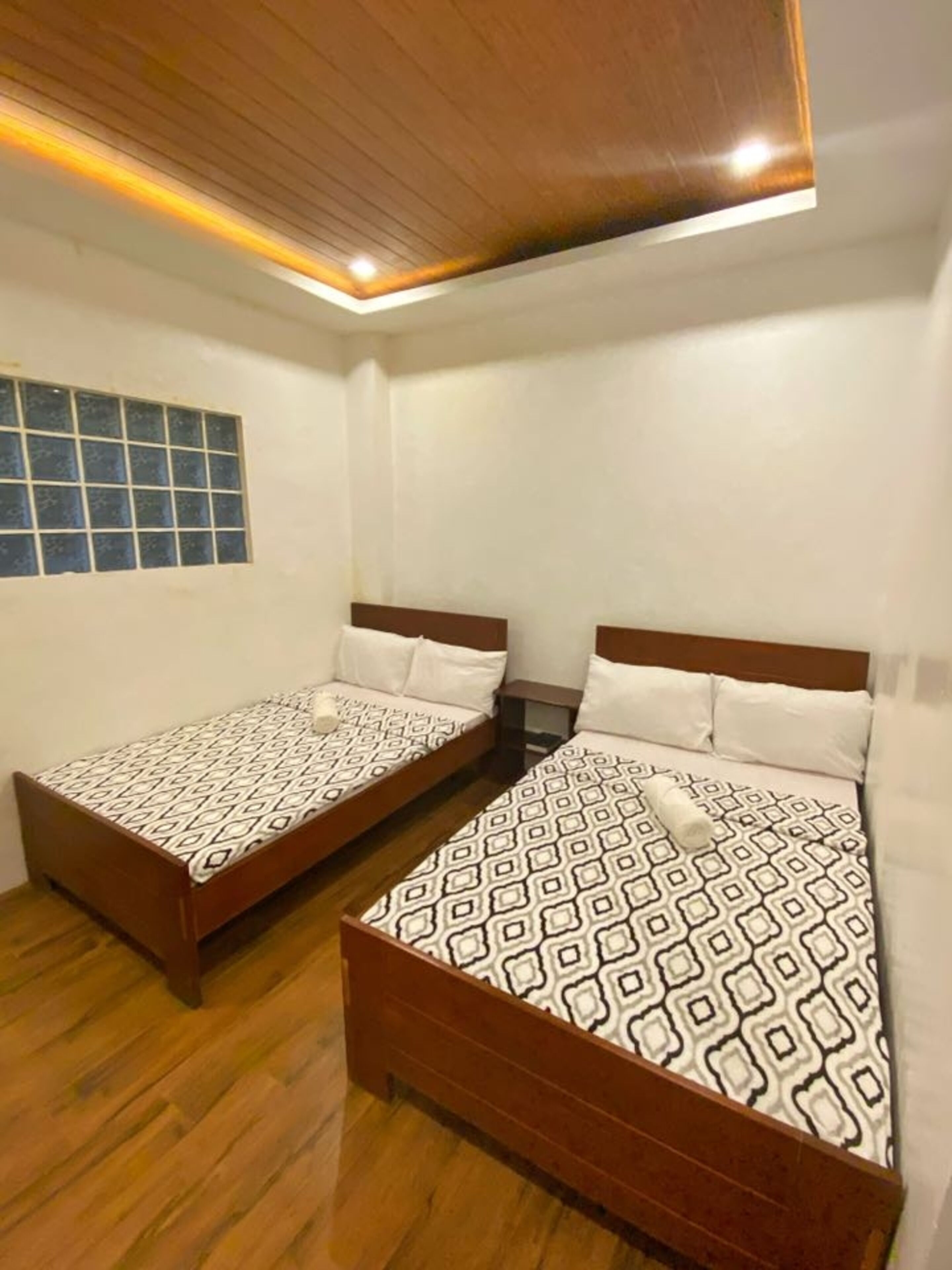 Una habitación con dos camas de madera, una ventana con diseño de cuadrícula y un techo de madera con iluminación empotrada.