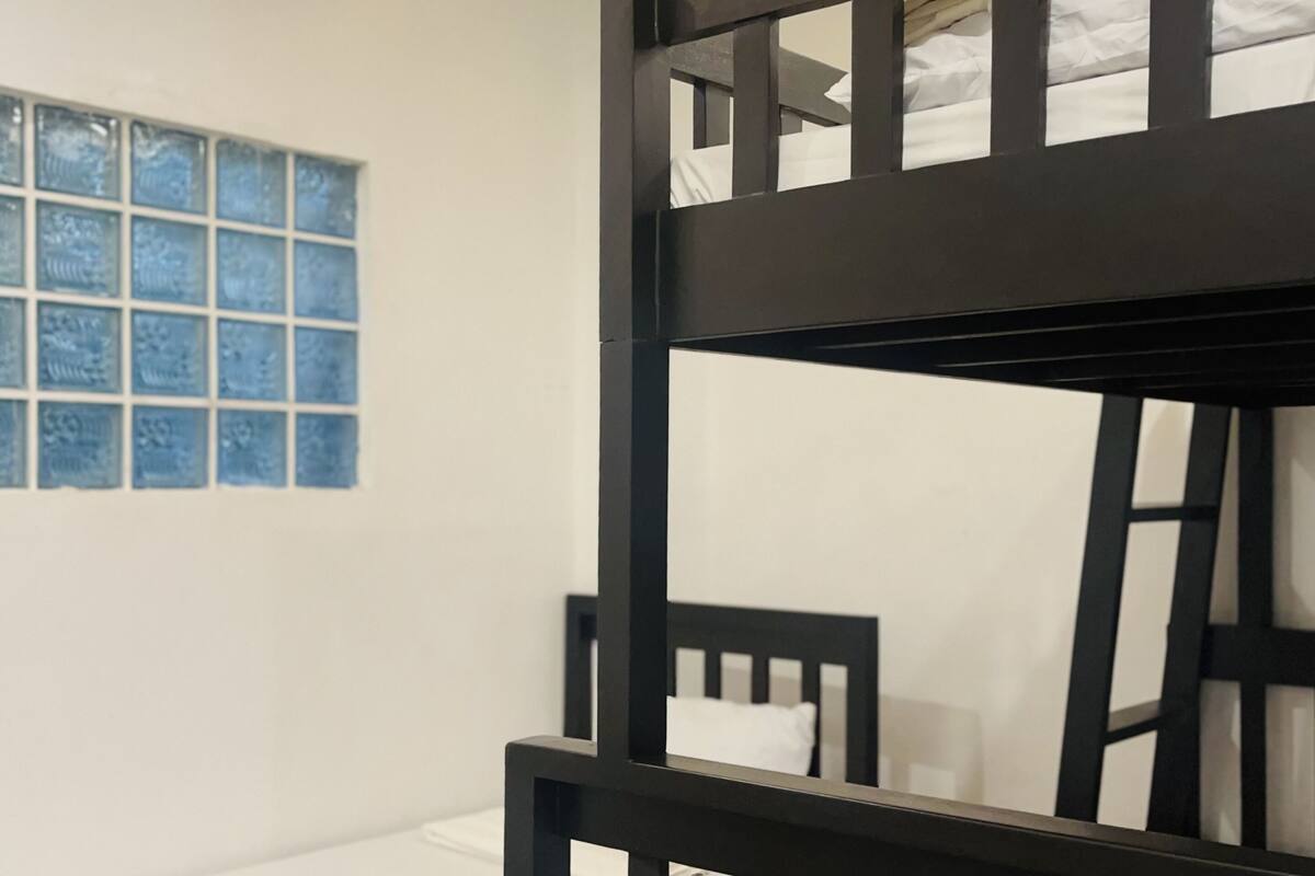 A bunk bed with white bedding, a window with blue-tinted glass, and a wooden ceiling with a yellow light strip.