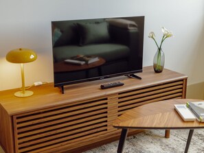 Ein Flachbildfernseher auf einem Holz-TV-Möbel mit Fernbedienung, einer Lampe und einer Vase mit Blumen.