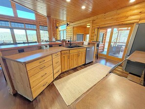 A log cabin interior with a kitchen featuring wooden cabinets, a dishwasher, and large windows. - Reiser's Ridge Cabin (Custer)