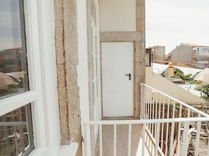 Ein Balkon mit weißer Tür und Geländer, mit Blick auf eine Wohngegend mit Häusern und Grünflächen.