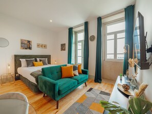 Ein modernes Schlafzimmer mit einem Bett, einem grünen Sofa, einem Schreibtisch mit einer Vase und einem großen Fenster mit Vorhängen.