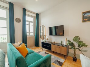 A living room with a teal sofa, a black entertainment unit, a flat-screen TV, and a large window with curtains. - Apartment  by Interhome (Porto)