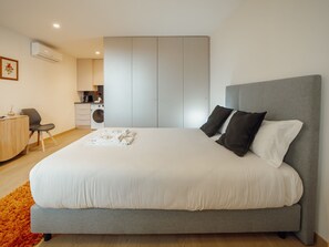Ein modernes Schlafzimmer mit einem großen Bett, einem grauen Kopfteil und einem kleinen Schreibtisch mit Stuhl.