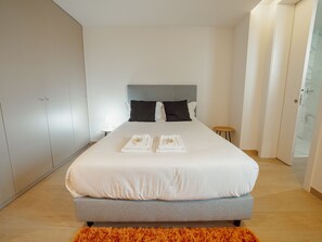 A modern bedroom with a large bed, grey headboard, white linens, and a small side table. - Apartment  by Interhome (Porto)