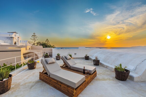 Terraza en la azotea con sillones de descanso, plantas en macetas y vistas al atardecer.