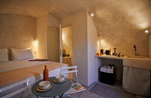 Ein Schlafzimmer mit einem Bett, Nachttisch mit zwei Schalen, einem kleinen Tisch mit einem Buch, einem Spiegel und einer Waschtischumgebung mit Pflegeartikeln.