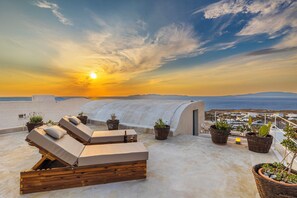 Una terrazza sul tetto con poltrone prendisole, piante in vaso e vista sul mare al tramonto.