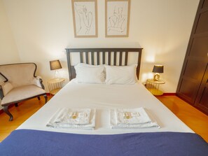 Une chambre d’hôtel avec un grand lit, deux tables de chevet, une chaise et des œuvres d’art accrochées au mur.