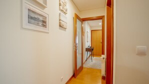 Um corredor com quadros nas paredes, piso de madeira e uma porta que dá para outro cômodo.