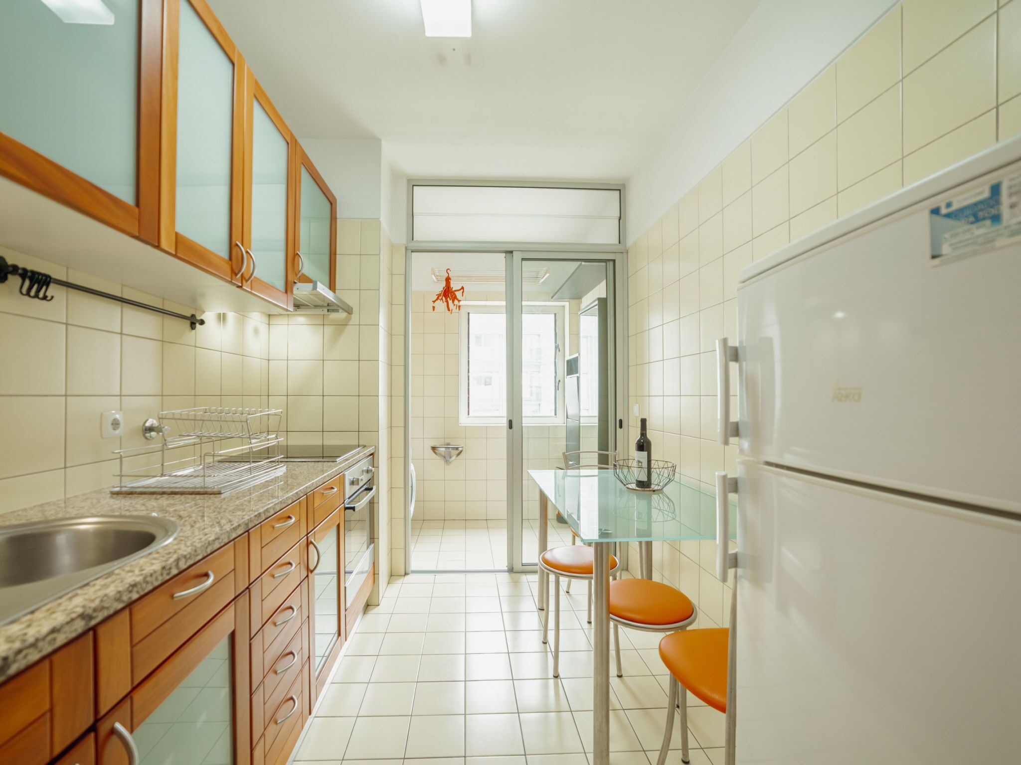 A kitchen with a refrigerator, oven, sink, and a glass dining table with chairs.