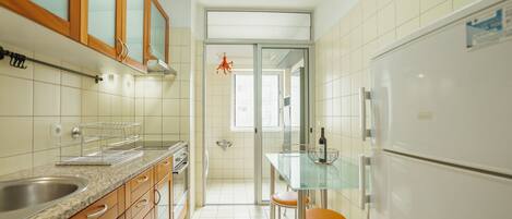 A kitchen with a refrigerator, oven, sink, and a glass dining table with chairs.