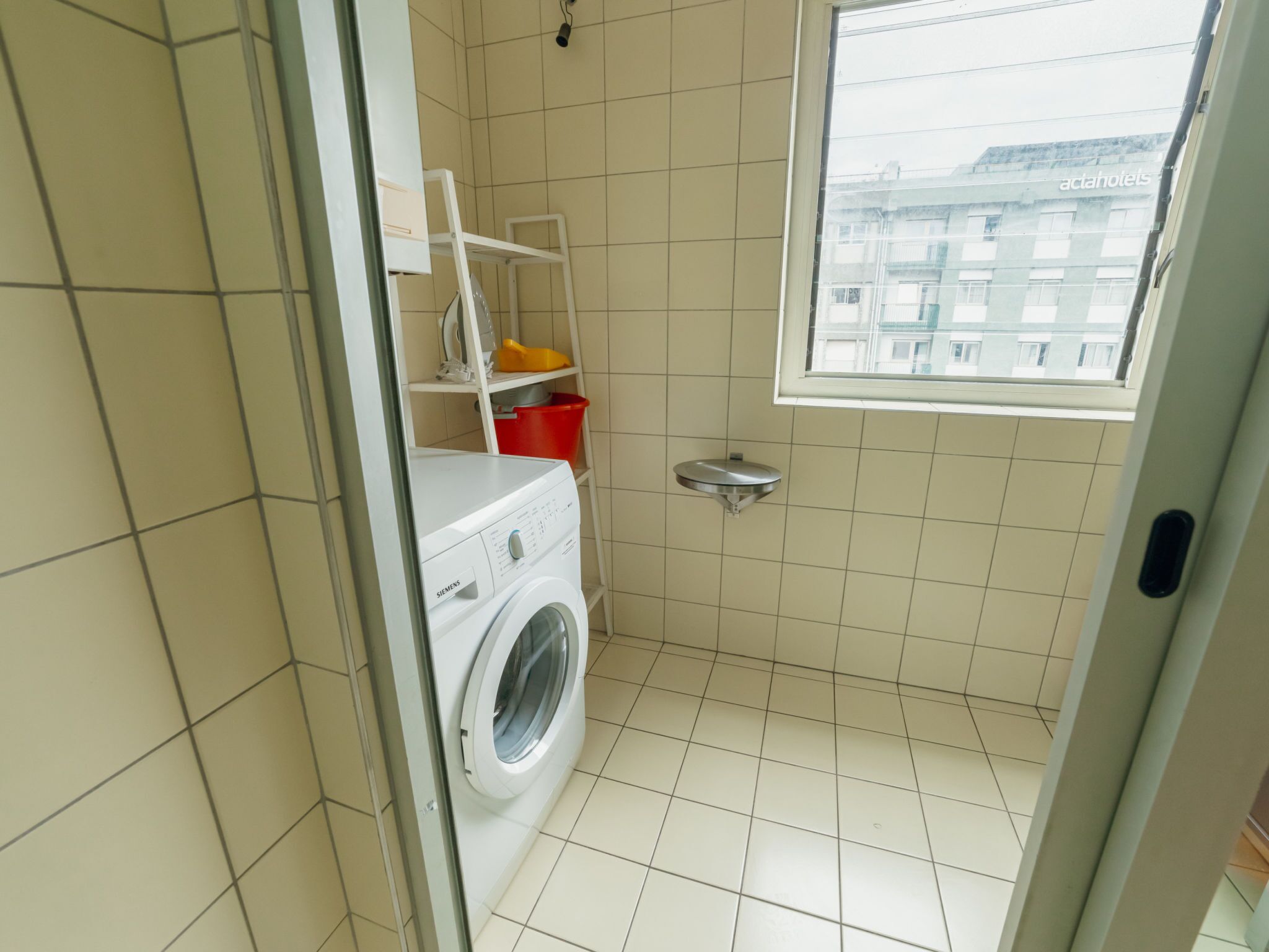 Un lavadero pequeño con una lavadora Siemens, un tendedero y una ventana.