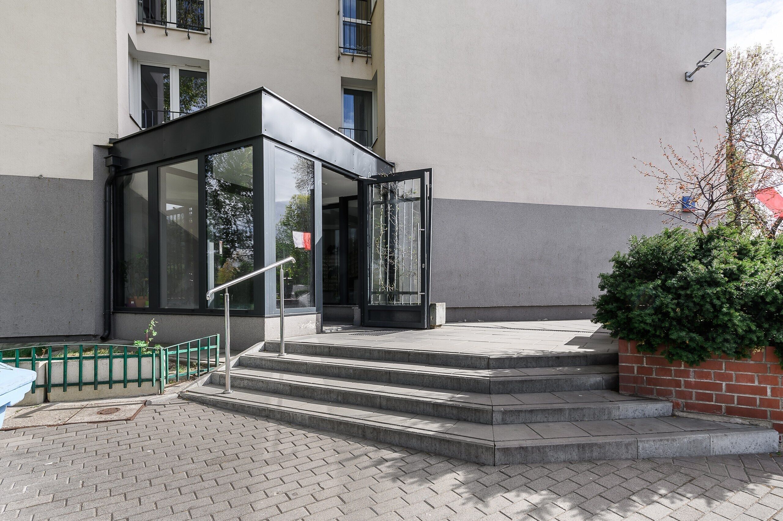 Une entrée moderne avec une porte en verre, des marches et une rambarde verte.